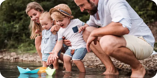 Family playing with paper boats along the waters edge